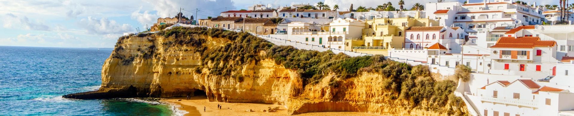 Wide sandy beach between cliffs and in front of charming white architecture in Carvoeiro, Algarve, Portugal