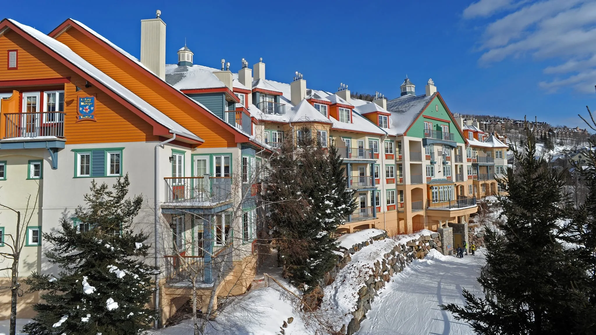 Row of brightly colored mountain townhouses with snow-covered roofs under a clear blue sky on a sunny day.