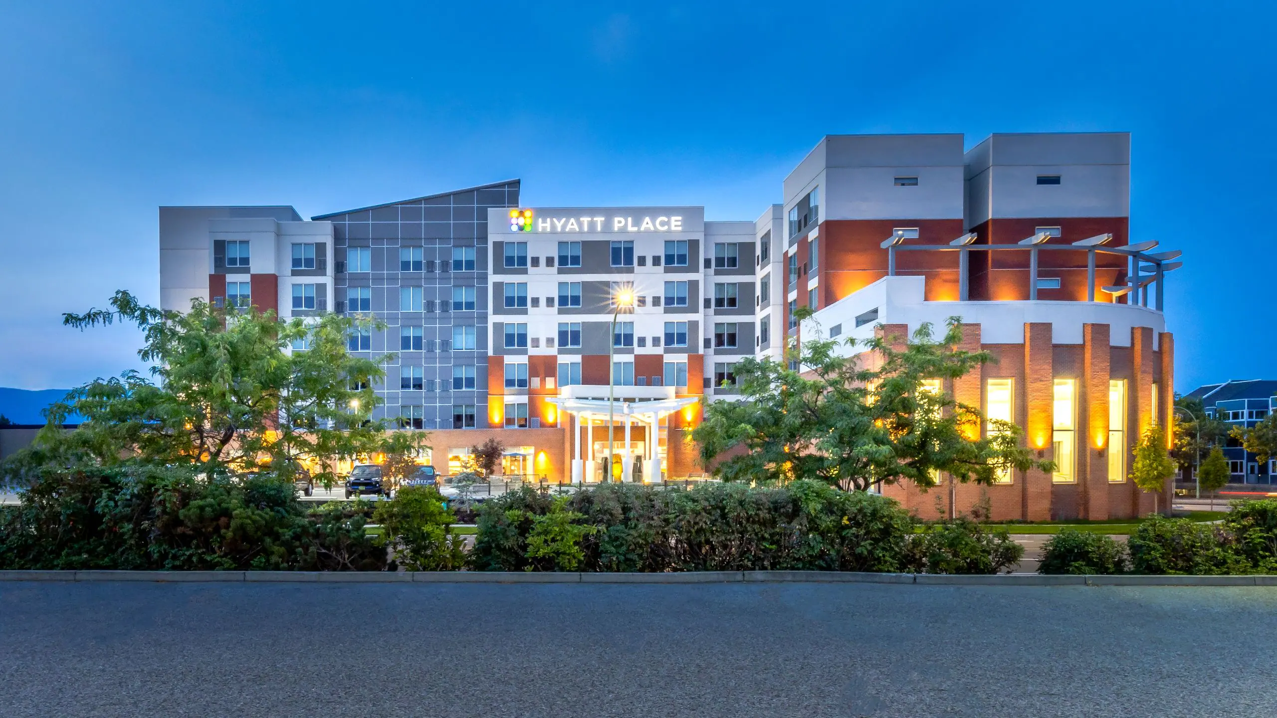 Hyatt Place hotel exterior at dusk with lit windows and landscaped foreground, blue sky above