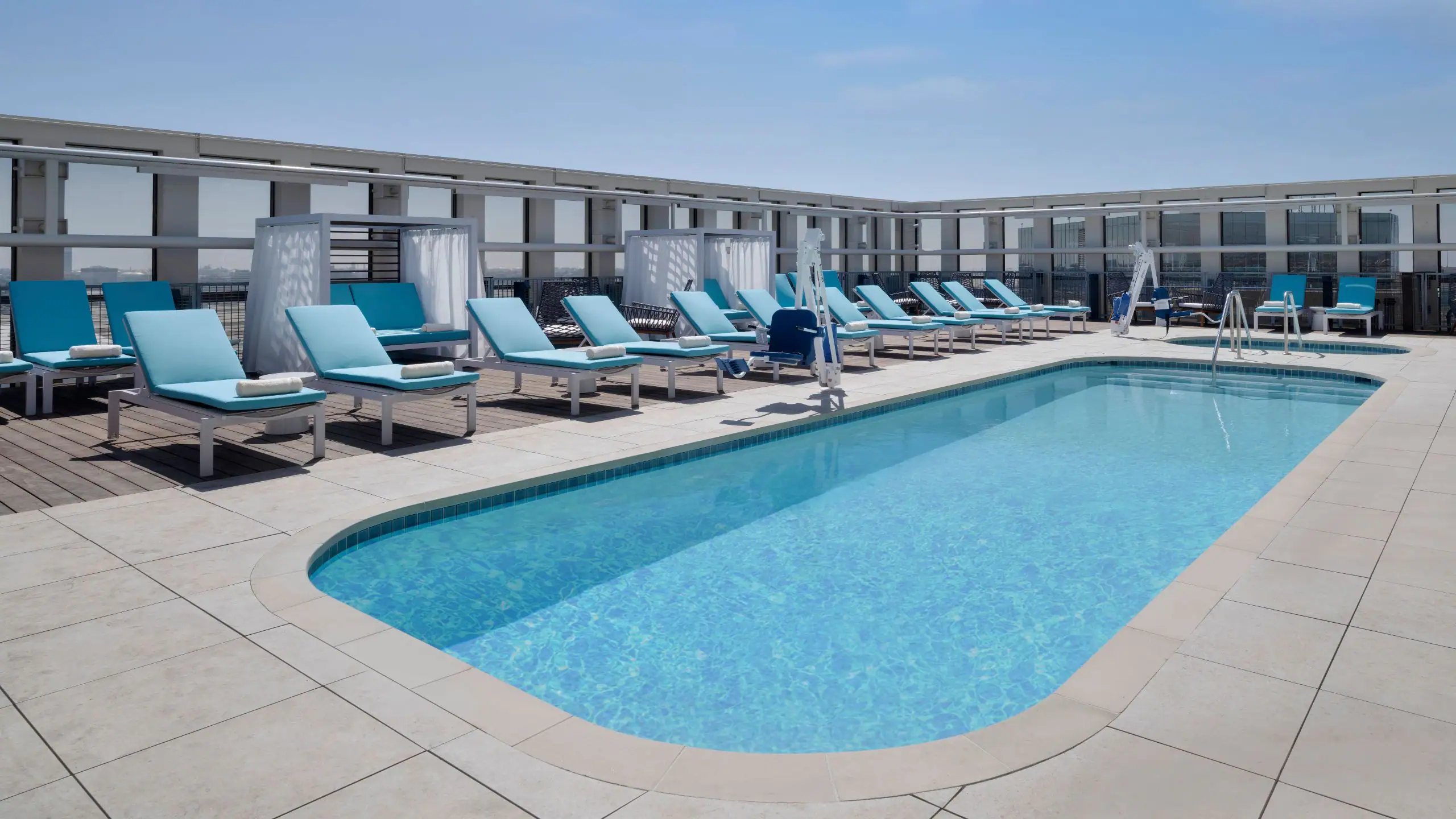 Rooftop pool area with blue lounge chairs and cabanas along a deck on a sunny day.