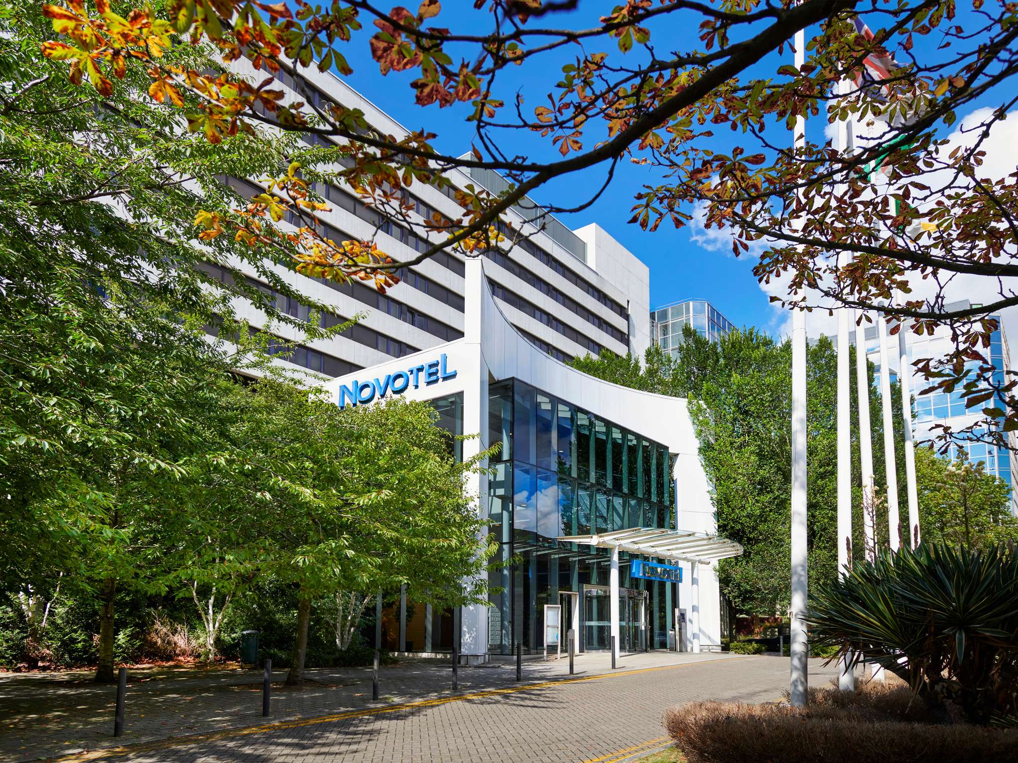 Novotel hotel building framed by green trees on a sunny day with a blue sky