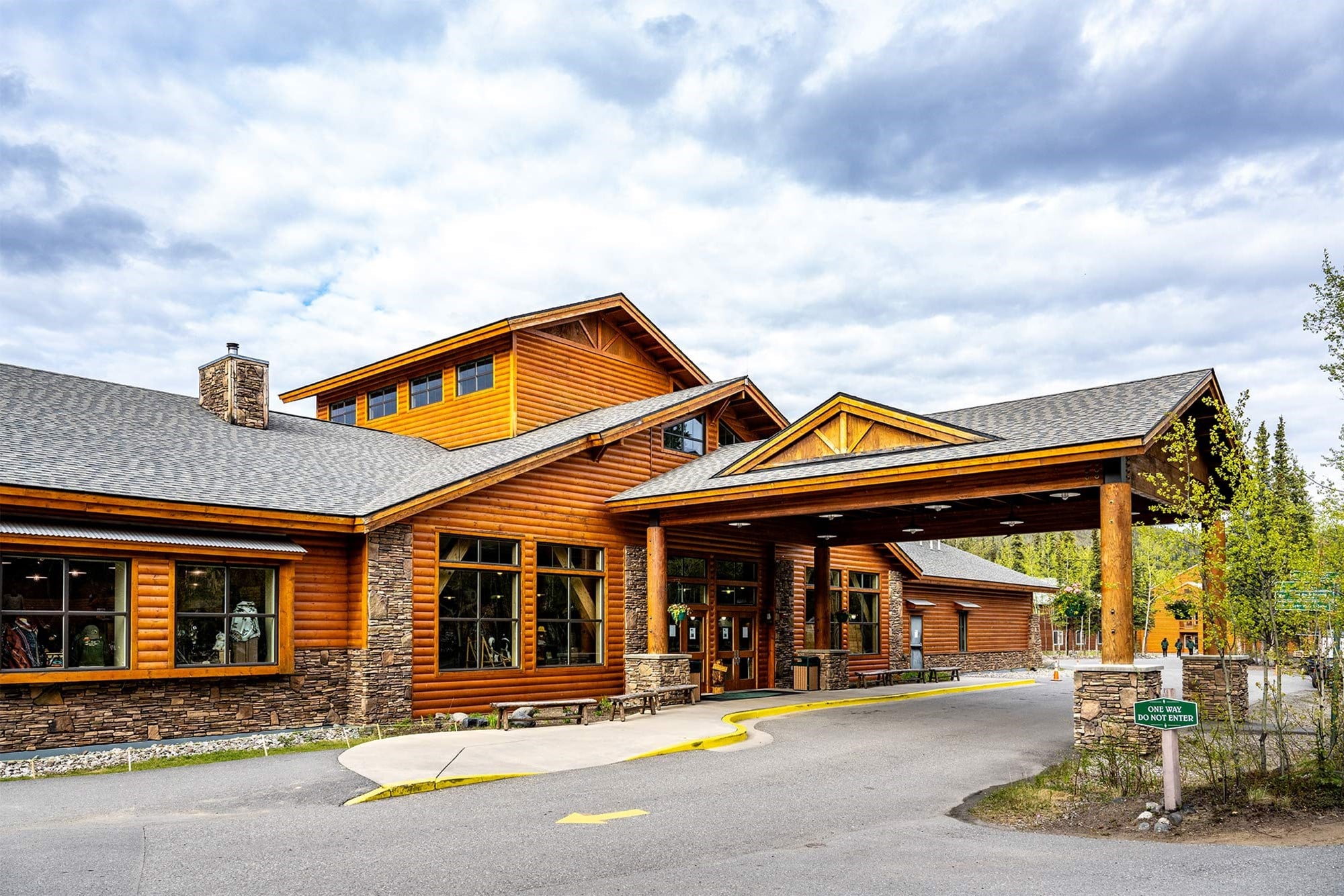 Lodge-style wooden building with stone accents, large windows, and a covered entrance under a cloudy sky; a one-way sign is in the foreground.