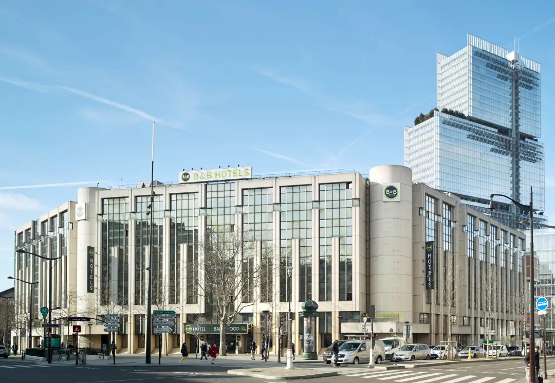 Front view of a beige hotel with tall vertical windows, signage reading 'B&B Hotels', on a busy city street.