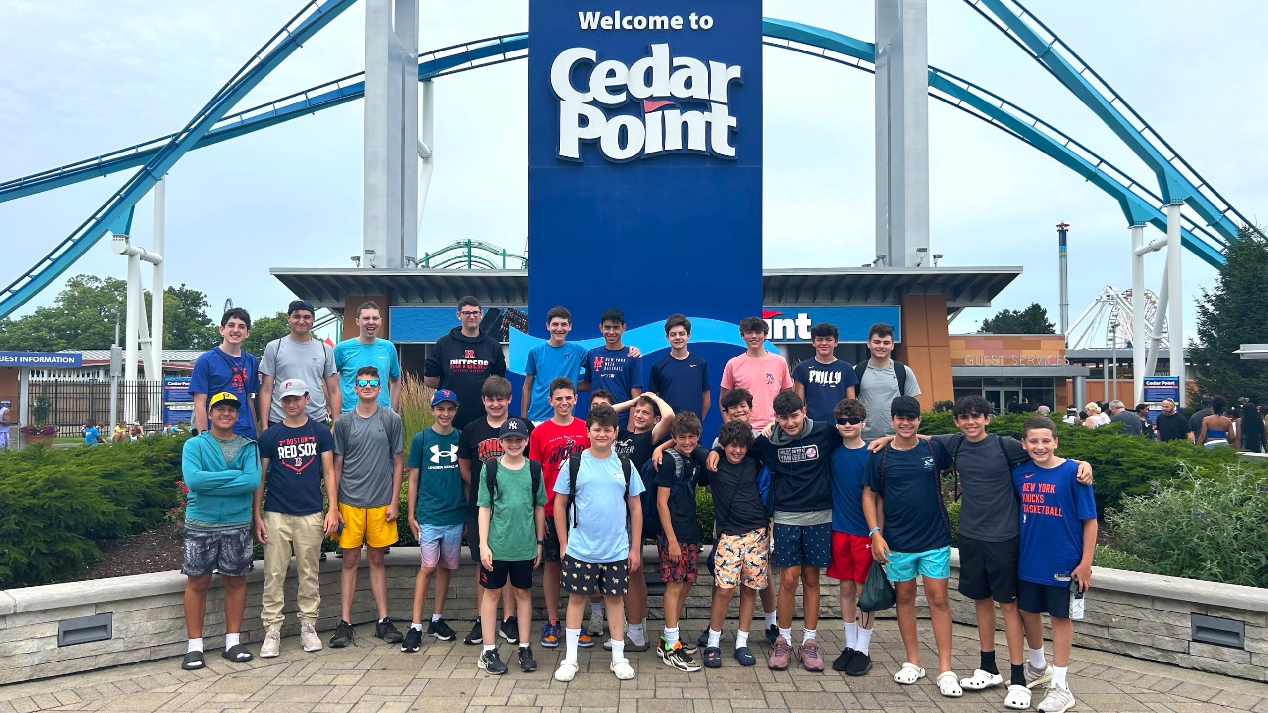 Group of smiling kids posing in front of the blue Cedar Point sign with roller coasters in the background.