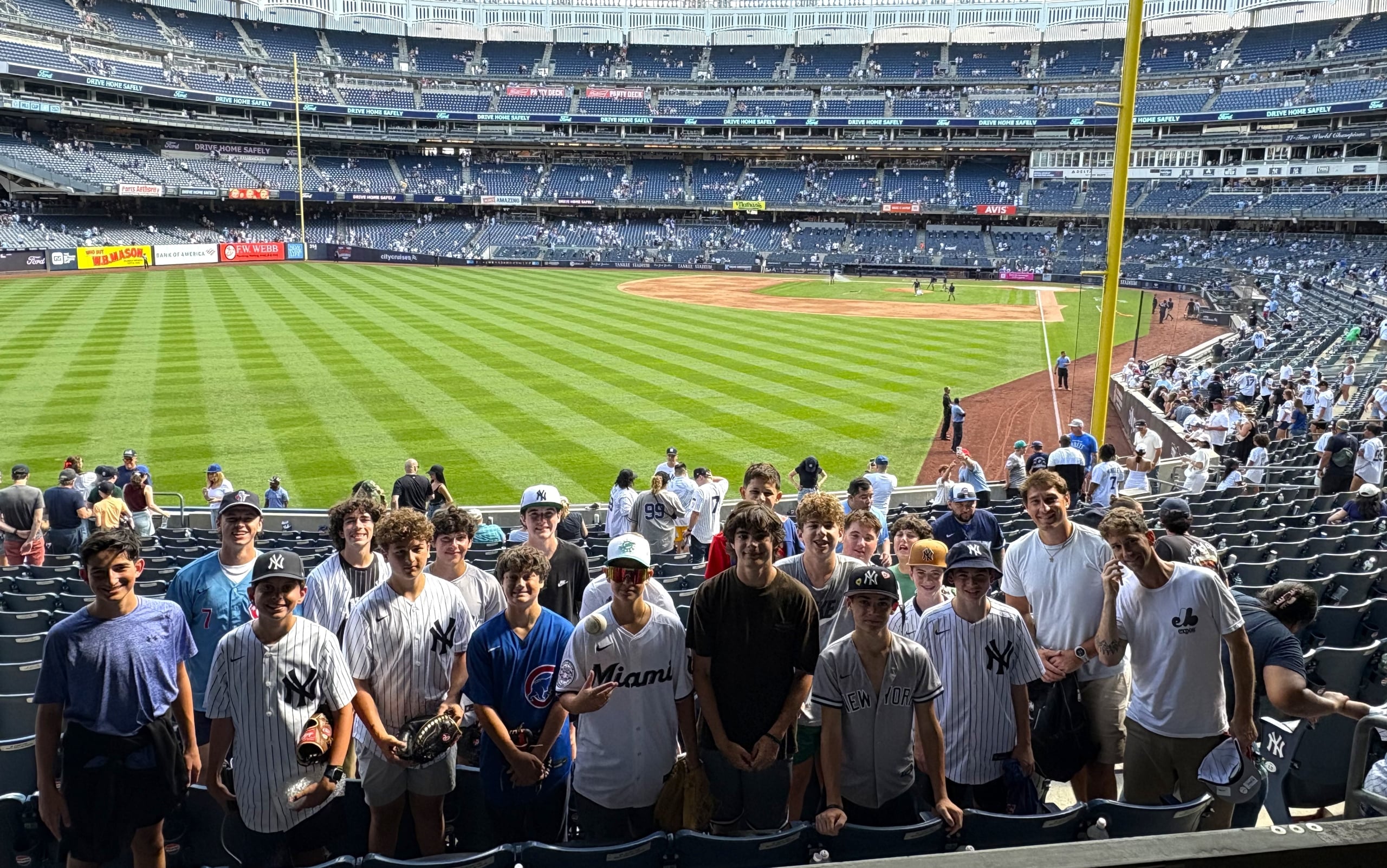Group of fans in white pinstriped baseball jerseys posing for a photo at a large stadium, with the field and dugout in the background.