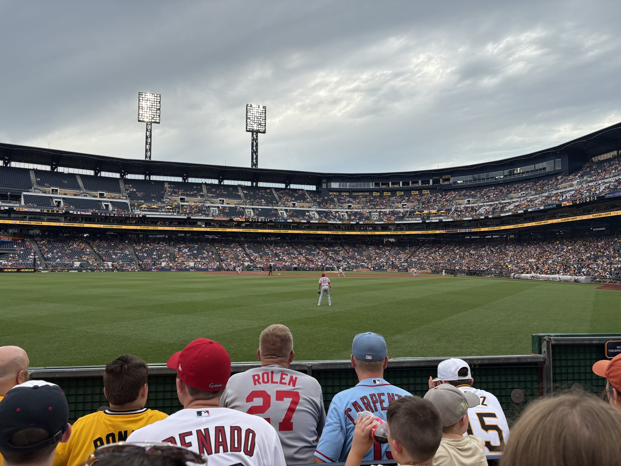 Baseball stadium filled with spectators; players on the diamond under an overcast sky.