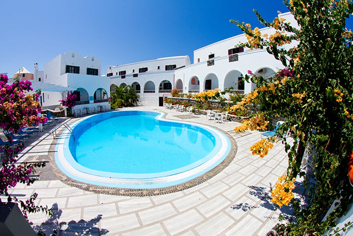 White Mediterranean-style hotel courtyard with a circular blue swimming pool and blooming bougainvillea strands in the foreground.