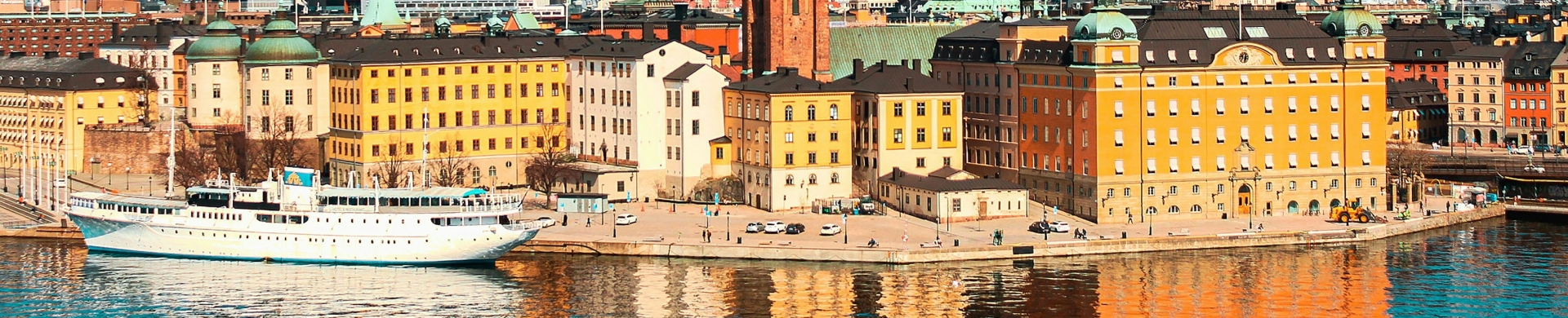 Colorful historic harbor with yellow, orange buildings along a quay and a white passenger ship docked by the water, reflections shimmering on the surface